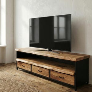 Puede incluir: Un mueble de televisi&oacute;n rectangular con una superficie de madera natural de borde vivo y un estante abierto a juego. La base est&aacute; construida en metal negro e incluye tres cajones de madera con tiradores negros, sosteniendo un televisor grande.
