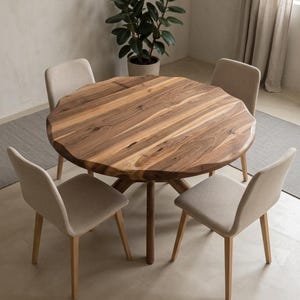 May include: A round wooden dining table with a natural edge, surrounded by four beige upholstered chairs. The table is approximately 48 inches in diameter. A potted plant is in the background, creating a warm and inviting dining space.