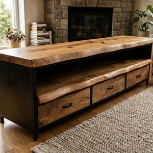 May include: A wooden media console with a natural wood top and three drawers. The console has a black metal frame and sits on a neutral-colored rug. The room features a fireplace and a window.