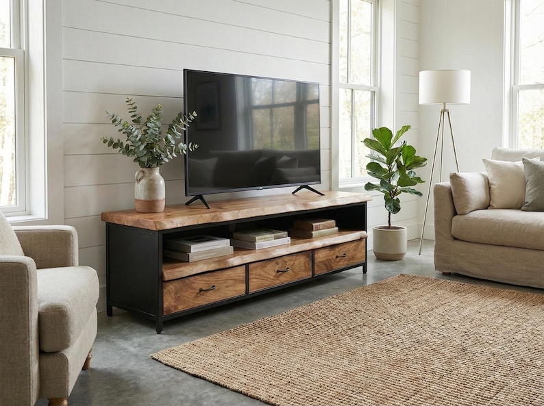 Puede incluir: Un mueble de televisi&oacute;n rectangular con una superficie de madera natural de borde vivo y una estructura de metal negro. La unidad incluye un estante de almacenamiento abierto y tres cajones inferiores con herrajes de metal oscuro.