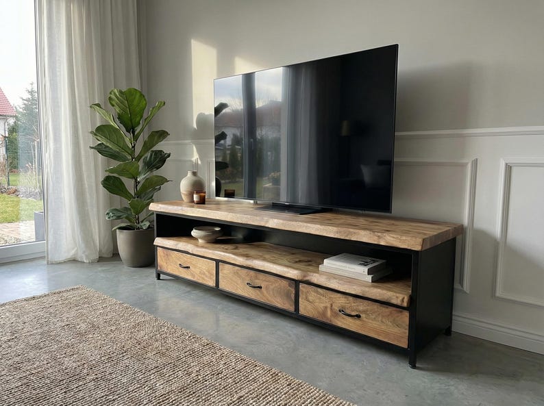 Puede incluir: Un mueble de televisi&oacute;n rectangular largo con una superficie de madera natural de borde vivo y tres cajones con marcos y tiradores de metal negro. La unidad incluye un estante abierto para almacenamiento y se apoya sobre una base de metal negro.