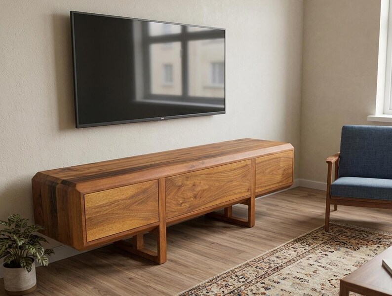 Puede incluir: Un mueble de TV moderno de madera con tres cajones y forma rectangular. El mueble est&aacute; hecho de madera de tonos c&aacute;lidos y est&aacute; sostenido por patas anguladas. Un televisor de pantalla plana negro grande est&aacute; montado encima.