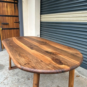 Pu&ograve; includere: Un grande tavolo ovale in legno con finitura in legno naturale. Il tavolo ha un piano spesso e solido e quattro gambe robuste. Il tavolo &egrave; in legno con una bella venatura.