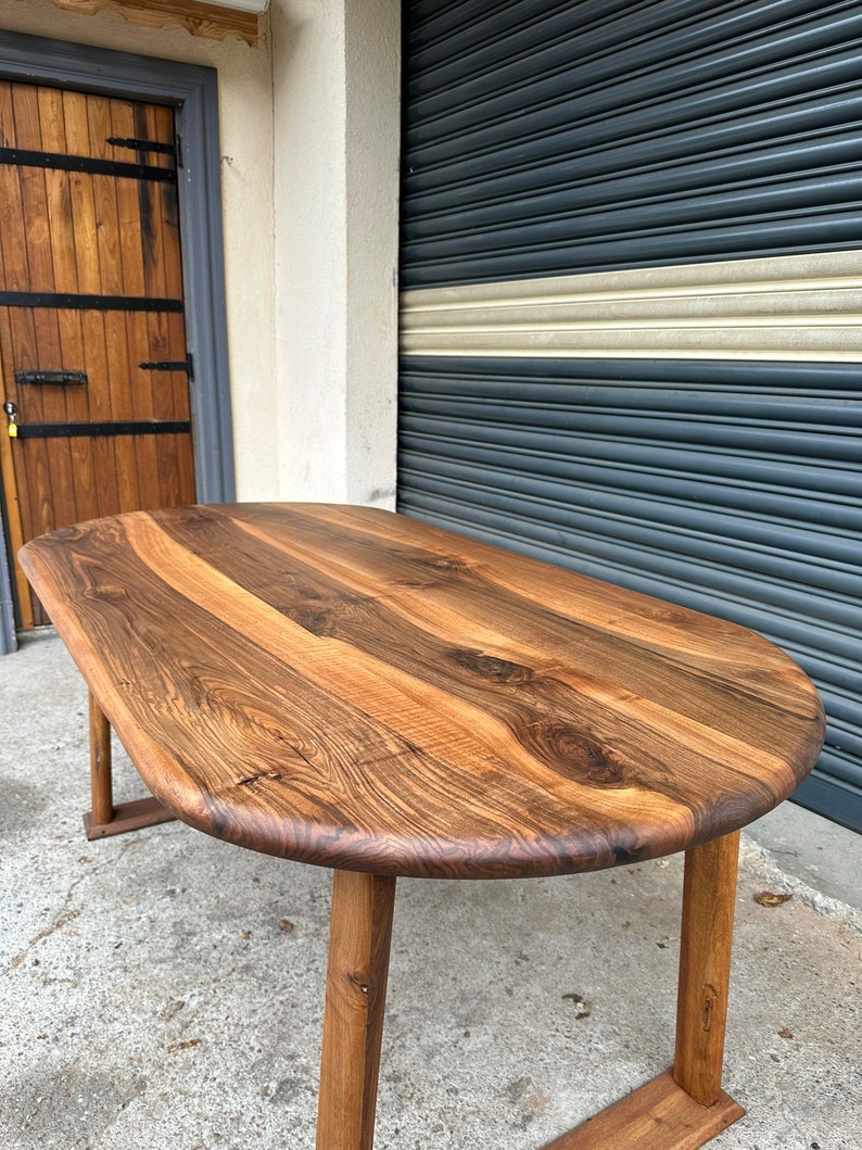 Pu&ograve; includere: Un grande tavolo ovale in legno con finitura in legno naturale. Il tavolo ha un piano spesso e solido e quattro gambe robuste. Il tavolo &egrave; in legno con una bella venatura.