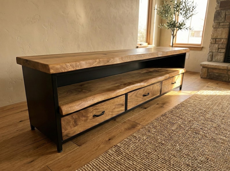 Puede incluir: Un mueble multimedia bajo con una superficie de madera natural de borde vivo y un estante abierto a juego. La base est&aacute; construida en metal negro e incluye tres cajones con tiradores negros delgados, ofreciendo espacio de almacenamiento.