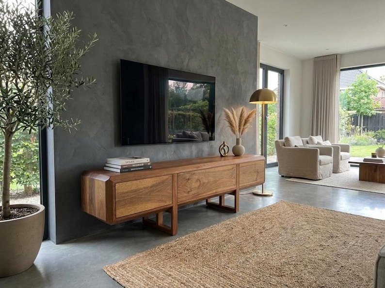Puede incluir: Sal&oacute;n moderno con un televisor grande y oscuro montado sobre una consola de medios de madera. La consola tiene tres cajones y un dise&ntilde;o minimalista. Una alfombra decorativa y una planta en maceta a&ntilde;aden calidez al espacio. La consola mide unos 180 cm.