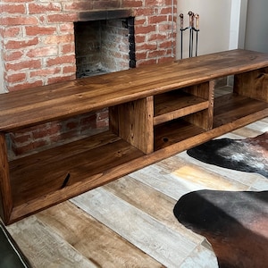 May include: A dark brown wooden TV stand with open shelves and a solid top. The stand has a rustic look and is made of reclaimed wood.