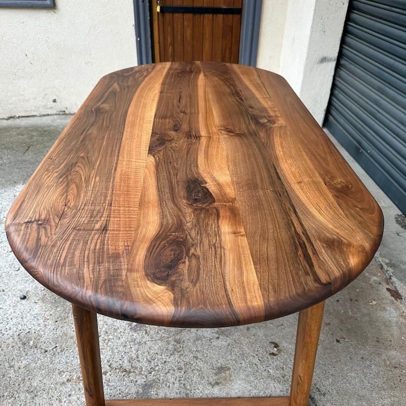 Pu&ograve; includere: Un grande tavolo ovale in legno con una finitura in legno marrone scuro. Il piano del tavolo &egrave; in legno massello e ha un aspetto naturale e rustico.