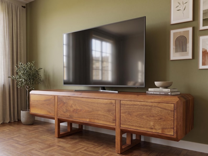 Puede incluir: Un televisor grande con pantalla oscura se encuentra sobre una consola de medios baja de madera. La consola es de madera de tonos c&aacute;lidos con veta natural, con tres cajones. Se ve una peque&ntilde;a planta en maceta y obras de arte enmarcadas.