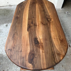 Pu&ograve; includere: Vista ravvicinata di un piano da tavolo ovale in legno di grandi dimensioni. Il piano del tavolo &egrave; in legno marrone scuro con una ricca venatura. Il legno ha una finitura naturale e sembra lucido.