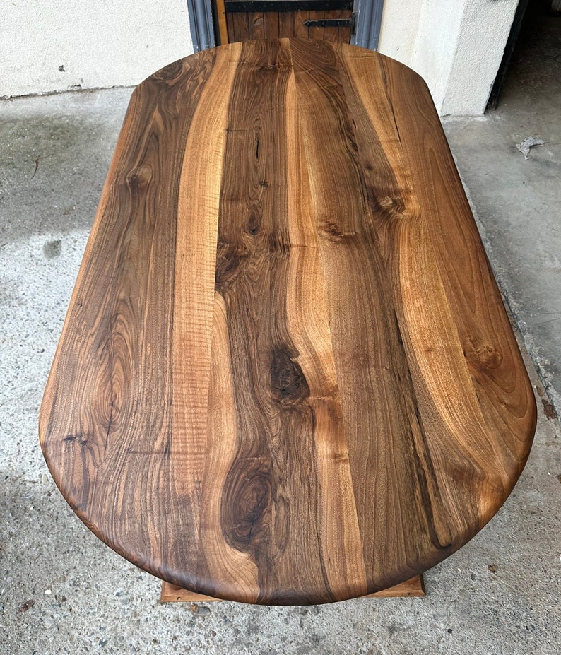 Pu&ograve; includere: Vista ravvicinata di un piano da tavolo ovale in legno di grandi dimensioni. Il piano del tavolo &egrave; in legno marrone scuro con una ricca venatura. Il legno ha una finitura naturale e sembra lucido.
