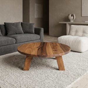 May include: A round coffee table crafted from natural brown wood with a visible grain pattern. The table features a circular top surface supported by three sturdy, angled wooden legs that extend outward from the center to provide stability.