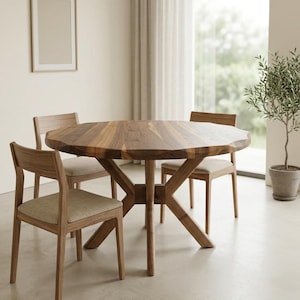 May include: A wooden dining table with a unique, multi-sided design, surrounded by four wooden chairs with beige upholstered seats. The table has a natural wood grain finish. A framed picture hangs on the wall, and a potted plant sits nearby.