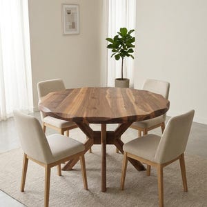 May include: A round wooden dining table with a unique, organic edge, surrounded by four beige upholstered chairs. The table is supported by a dark wood base. The chairs have light wood legs. The room has a neutral color palette.