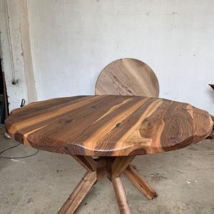 May include: A round wooden table with a natural edge and a starburst pattern on the tabletop. The table is supported by a wooden base with angled legs. The table is approximately 40 inches in diameter.