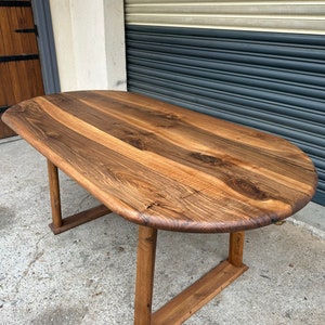 Pu&ograve; includere: Un grande tavolo ovale in legno con finitura in legno naturale. Il tavolo ha un design semplice e moderno con quattro gambe e un piano largo e piatto. Il tavolo &egrave; realizzato in legno massello e ha un aspetto rustico e artigianale.