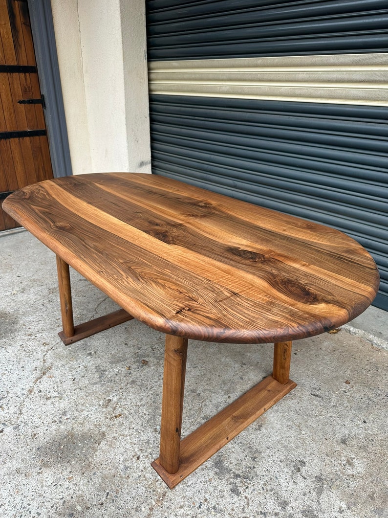 Pu&ograve; includere: Un grande tavolo ovale in legno con finitura in legno naturale. Il tavolo ha un design semplice e moderno con quattro gambe e un piano largo e piatto. Il tavolo &egrave; realizzato in legno massello e ha un aspetto rustico e artigianale.