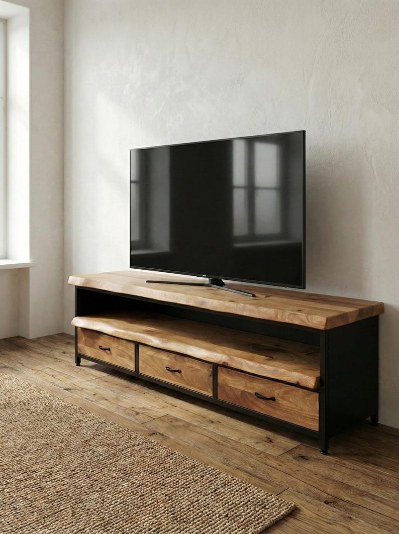 Puede incluir: Un mueble de televisi&oacute;n rectangular con una superficie de madera natural de borde vivo y un estante abierto a juego. La base est&aacute; construida en metal negro e incluye tres cajones de madera con tiradores negros, sosteniendo un televisor grande.