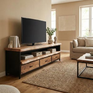 Puede incluir: Un mueble multimedia largo con una superficie y estante de madera natural de borde vivo, sostenido por un marco de metal negro. La unidad incluye tres cajones inferiores con tiradores de metal oscuro y un estante abierto con libros y cajas.