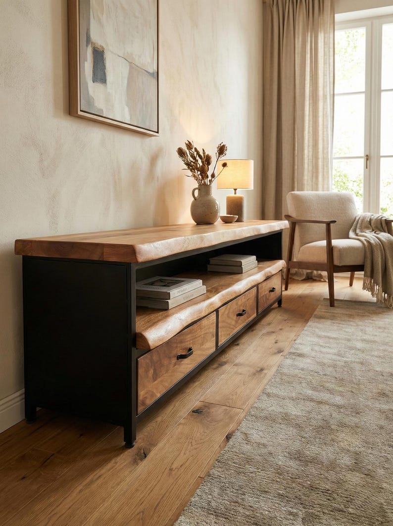 Puede incluir: Un mueble multimedia largo con estructura de metal negro y tres cajones con frentes de madera natural de borde vivo. La unidad incluye un estante abierto para almacenamiento y una superficie superior gruesa de madera a juego.