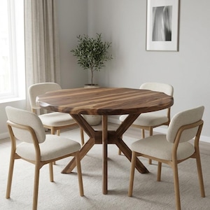 May include: A round wooden dining table with a natural finish, supported by a unique base, surrounded by four beige upholstered chairs. The table is approximately 48 inches in diameter, creating a warm and inviting dining space.