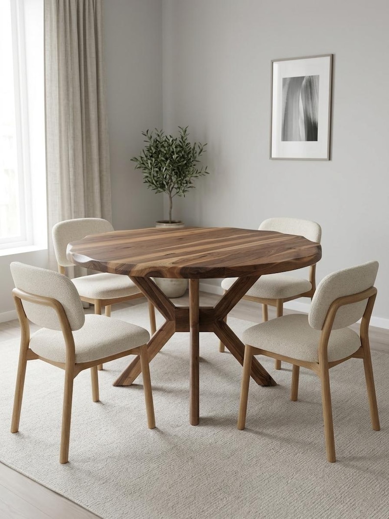 May include: A round wooden dining table with a natural finish, supported by a unique base, surrounded by four beige upholstered chairs. The table is approximately 48 inches in diameter, creating a warm and inviting dining space.