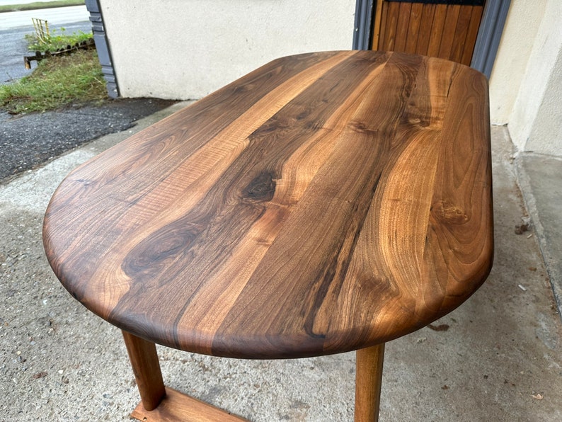 Pu&ograve; includere: Primo piano di un piano da tavolo ovale in legno marrone scuro con una venatura naturale del legno. Il piano del tavolo &egrave; liscio e lucido.