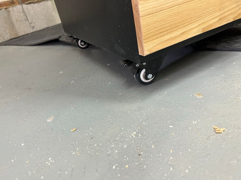 May include: A black and wood cabinet with four black wheels. The cabinet is on a gray concrete floor.