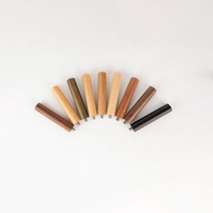 Op de afbeelding: Een verzameling van negen houten meubelpoten in verschillende tinten bruin, beige en zwart, gerangschikt in een halve cirkel. Elke poot heeft een cilindrische vorm met een metalen basis.