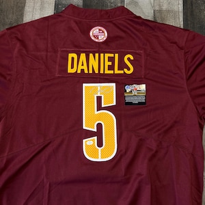 Puede incluir: Camiseta de fútbol granate con el nombre "DANIELS" y el número "5" en amarillo. La camiseta tiene un contorno blanco alrededor del número. Un parche con el logo del equipo es visible en la parte superior. Una pequeña pegatina está en el lado derecho.