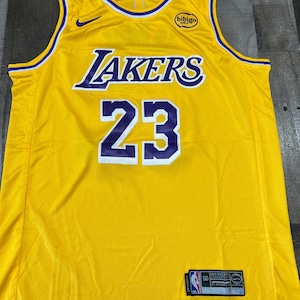 May include: A yellow Lakers basketball jersey with the number 23 in white and purple. The word "Lakers" is across the chest in purple and white. A small Nike swoosh is visible.