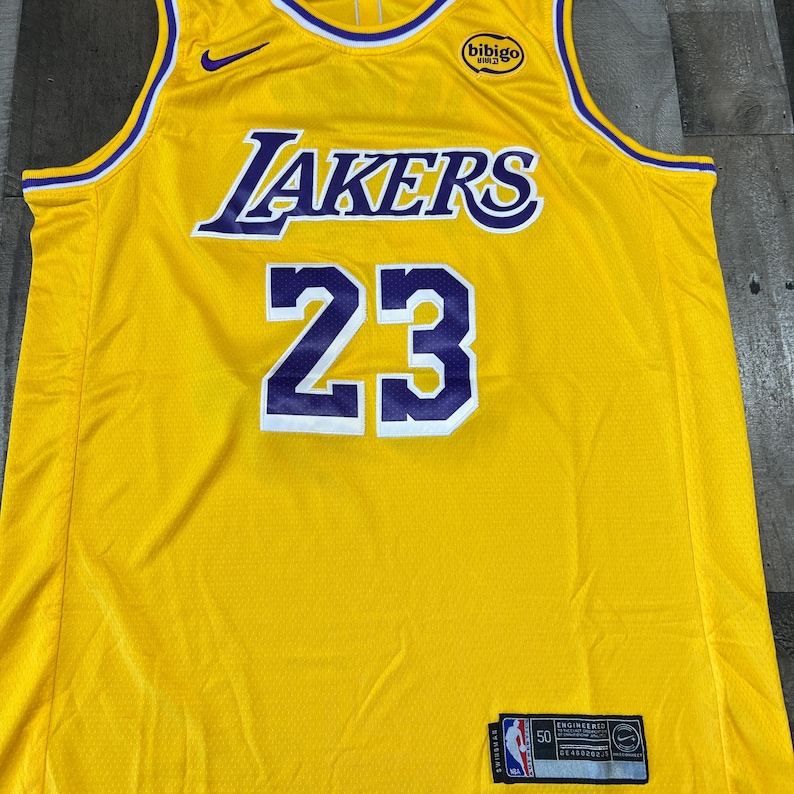 May include: A yellow Lakers basketball jersey with the number 23 in white and purple. The word "Lakers" is across the chest in purple and white. A small Nike swoosh is visible.