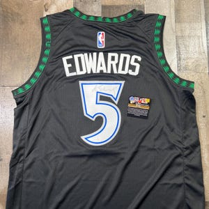 Może przedstawiać: Czarna koszulka do koszykówki z napisem "EDWARDS" i numerem "5" w kolorze białym z niebieskim obramowaniem. Koszulka ma zielone i białe wykończenia wzdłuż ramion i dekoltu. Widoczne jest logo NBA.