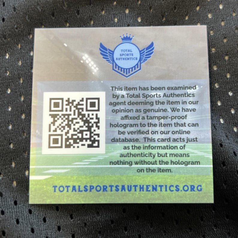 May include: A square card with the Total Sports Authentics logo, a QR code, and text about item authenticity. The card has a blue logo with wings and text that reads "TOTAL SPORTS AUTHENTICS". The text explains the item's authenticity.