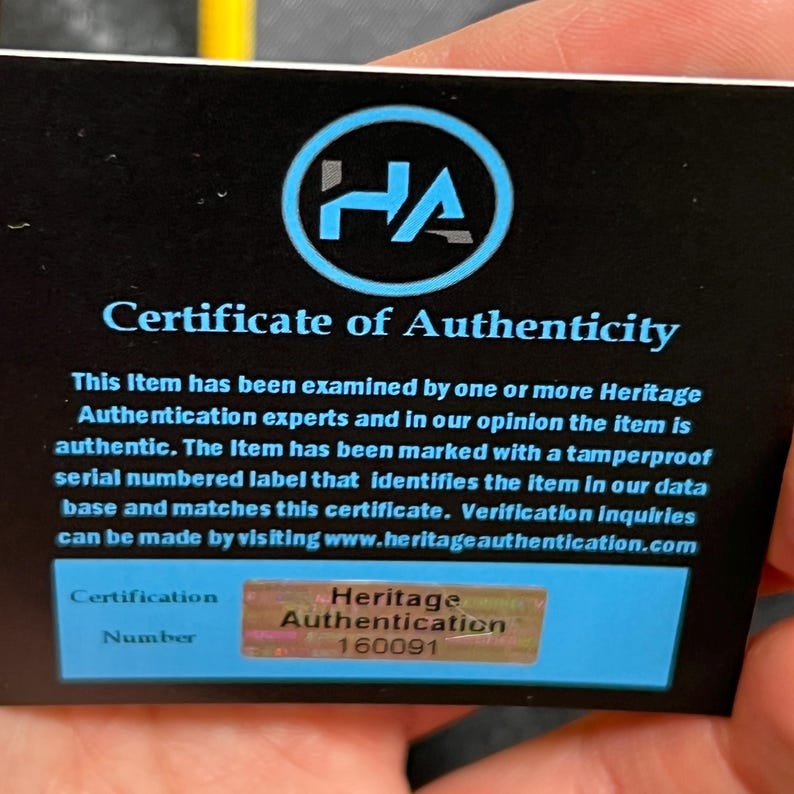 May include: A black rectangular Certificate of Authenticity card featuring a blue circular HA logo at the top. The text reads Certificate of Authenticity, followed by details about item verification and a holographic label with the number 160091.