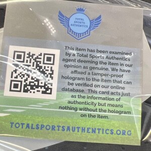 May include: A clear plastic bag containing a white and green Total Sports Authentics authenticity card. The card has a QR code, a blue logo with wings, and text stating the item has been examined and is deemed genuine. The website TOTALSPORTSAUTHENTICS.ORG is also visible.