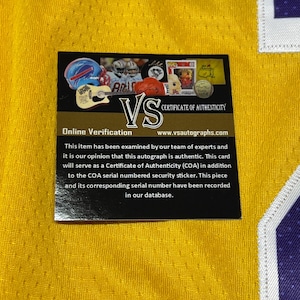 May include: A yellow jersey with a black and white certificate of authenticity. The certificate includes the text "VS" and "Certificate of Authenticity". The certificate also has the text "Online Verification" and "www.vsautographs.com".