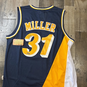 May include: A navy blue basketball jersey featuring the name MILLER and the number 31 in yellow with white trim on the back. The number 31 includes a black ink signature. A small rectangular authentication card is attached to the left side.