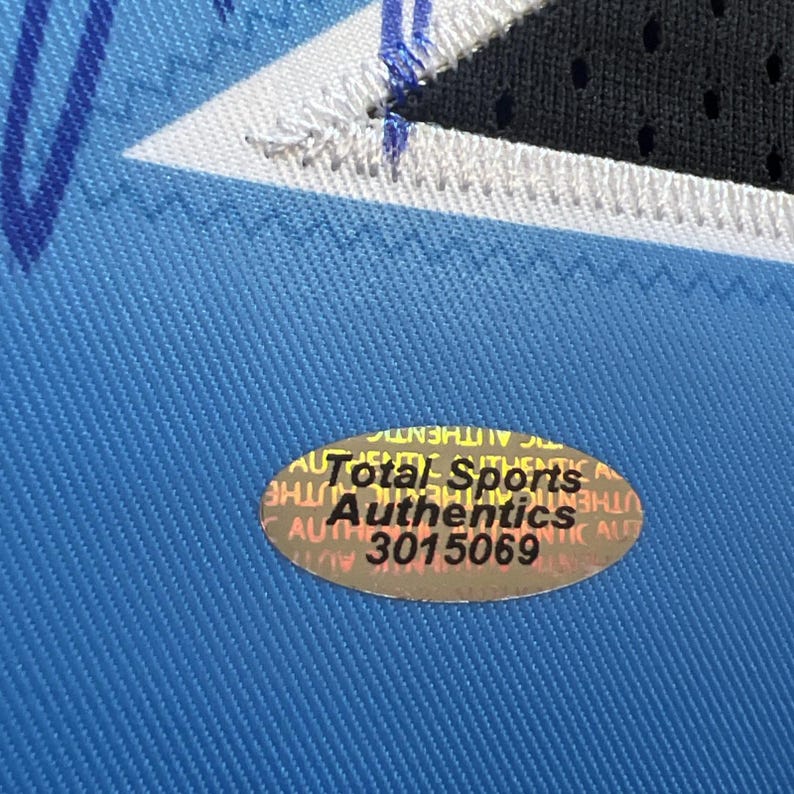 May include: Close-up of a blue jersey with a white and black design. A Total Sports Authentics sticker is affixed to the jersey, with the number 3015069 visible.