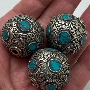 May include: Three silver and turquoise beads with intricate floral designs. Each bead has a hole for stringing.