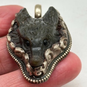 Peut inclure: Un pendentif en argent avec une tête de loup verte sculptée. Les yeux du loup sont noirs et le pendentif est entouré d'un motif en filigrane argenté.