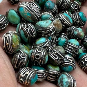 May include: A collection of turquoise and silver beads. The beads are oval shaped and have intricate silver designs. The turquoise is a vibrant blue-green color.
