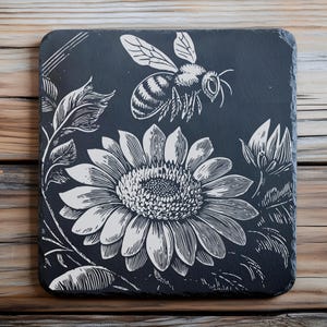 May include: Black slate coaster with a white and black engraved design of a sunflower and a bee.