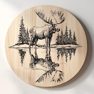 May include: A round wooden wall art piece featuring a detailed black and white illustration of a moose standing in water, with its reflection visible. The background includes pine trees and a shoreline, creating a nature-themed design.