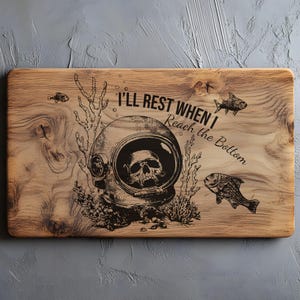May include: Wooden chopping board with a skull in a diving helmet design. The board features the text "I'll Rest When I Reach the Bottom" and illustrations of fish and coral. The wood grain is visible.