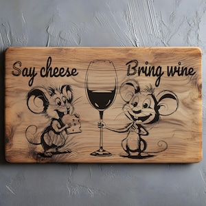 Op de afbeelding: Houten serveerplank met cartoonmuizen, één met kaas, de ander met een wijnglas. De tekst "Say cheese" en "Bring wine" zijn boven de illustraties gegraveerd. Een leuk keukenaccessoire.