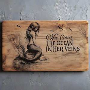 May include: Wooden rectangular sign with a mermaid illustration and the text "She Carries The Ocean In Her Veins." The mermaid is depicted with long flowing hair and a fish tail. The sign has a natural wood grain finish and includes flying birds.