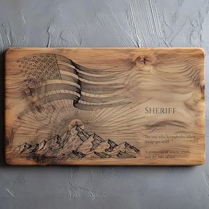 May include: Wooden cutting board with an engraved design featuring an American flag, mountains, and a sheriff's badge. The word "SHERIFF" is displayed with a definition. The board is rectangular and has a natural wood grain.