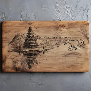 Puede incluir: Tabla de cortar de madera con una escena invernal grabada con láser. El diseño presenta un árbol de Navidad, montañas y un lago, con el texto "WHERE THE STARS ABOVE MEET THE LIGHTS BELOW". La tabla tiene vetas de madera natural.