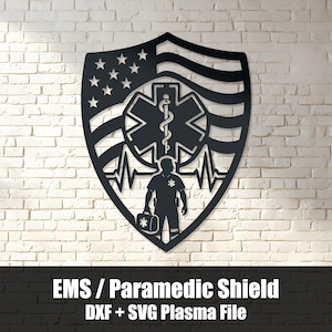 Peut inclure: Une décoration murale en métal noir en forme de bouclier, présentant une découpe du drapeau américain, le symbole médical de l'Étoile de Vie, une ligne d'électrocardiogramme et la silhouette d'un ambulancier portant une trousse médicale.